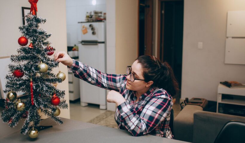 Karácsonyi készülődés otthon, nő karácsonyfát díszít gyertyafényben