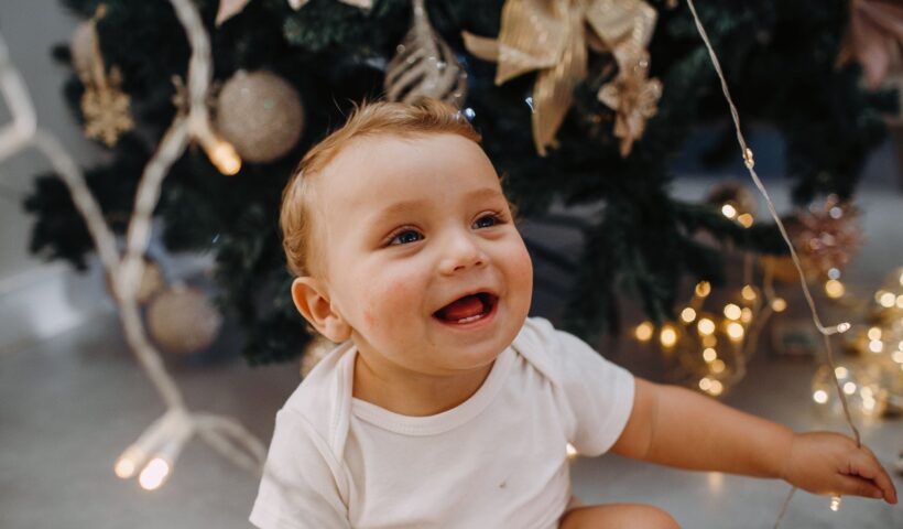 Ünnepi fotózás otthon, mosolygó gyermek díszített karácsonyfa mellett