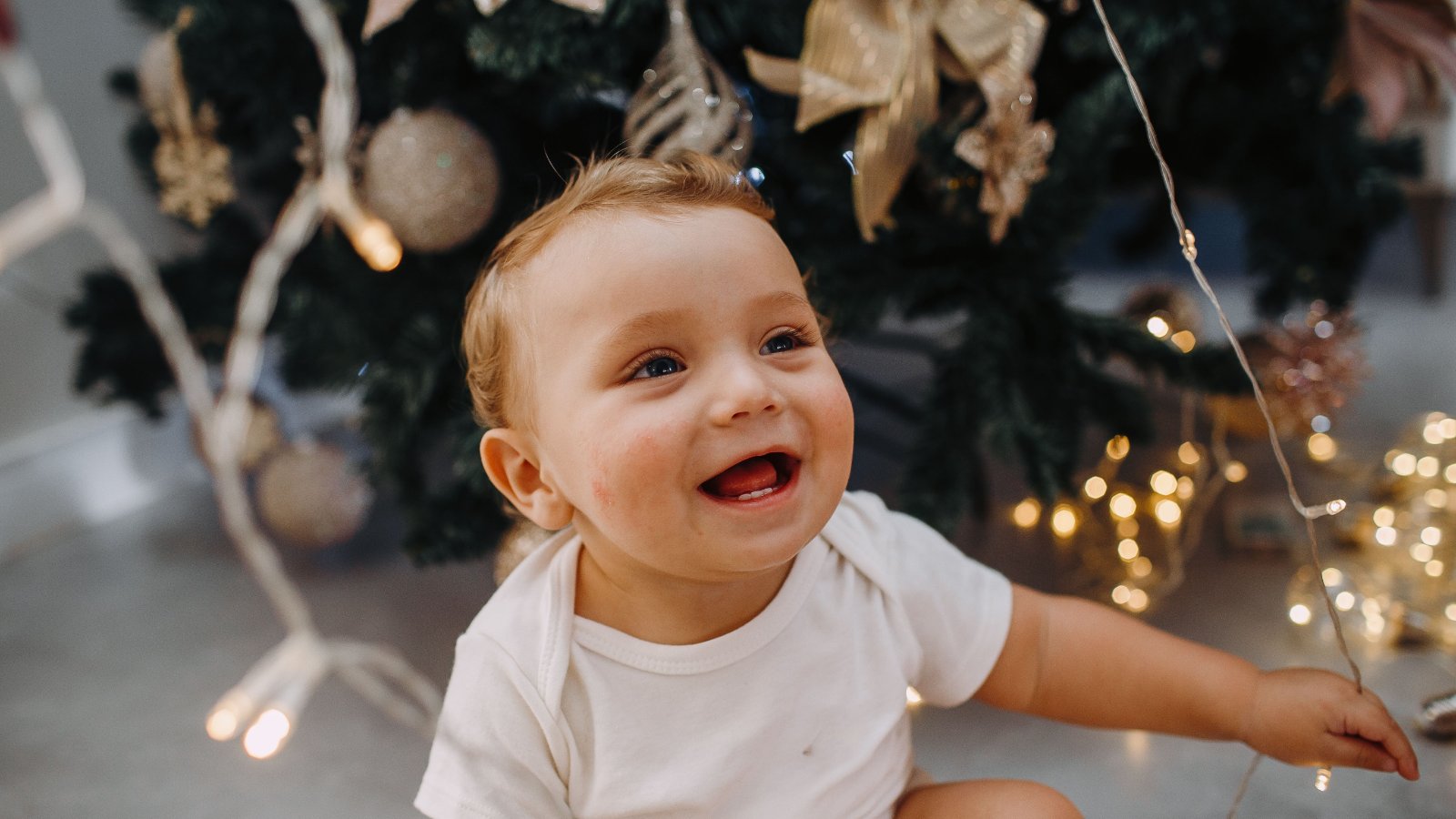 Ünnepi fotózás otthon, mosolygó gyermek díszített karácsonyfa mellett